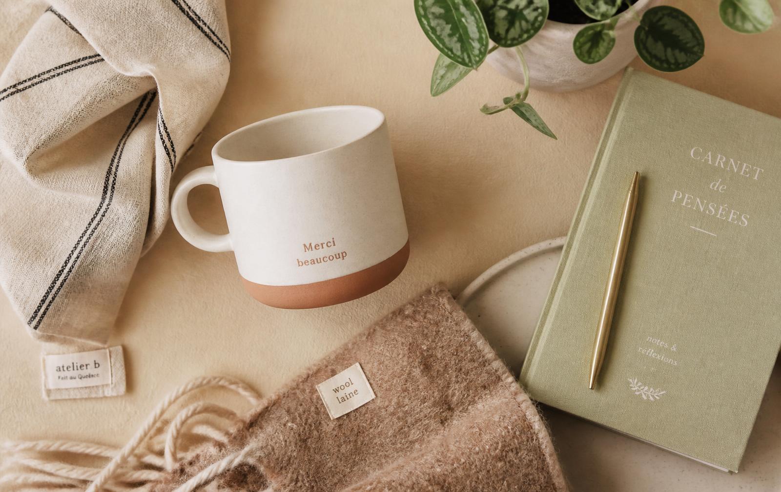 Tasse en grès, jeté de laine et carnet posés sur un fond sable